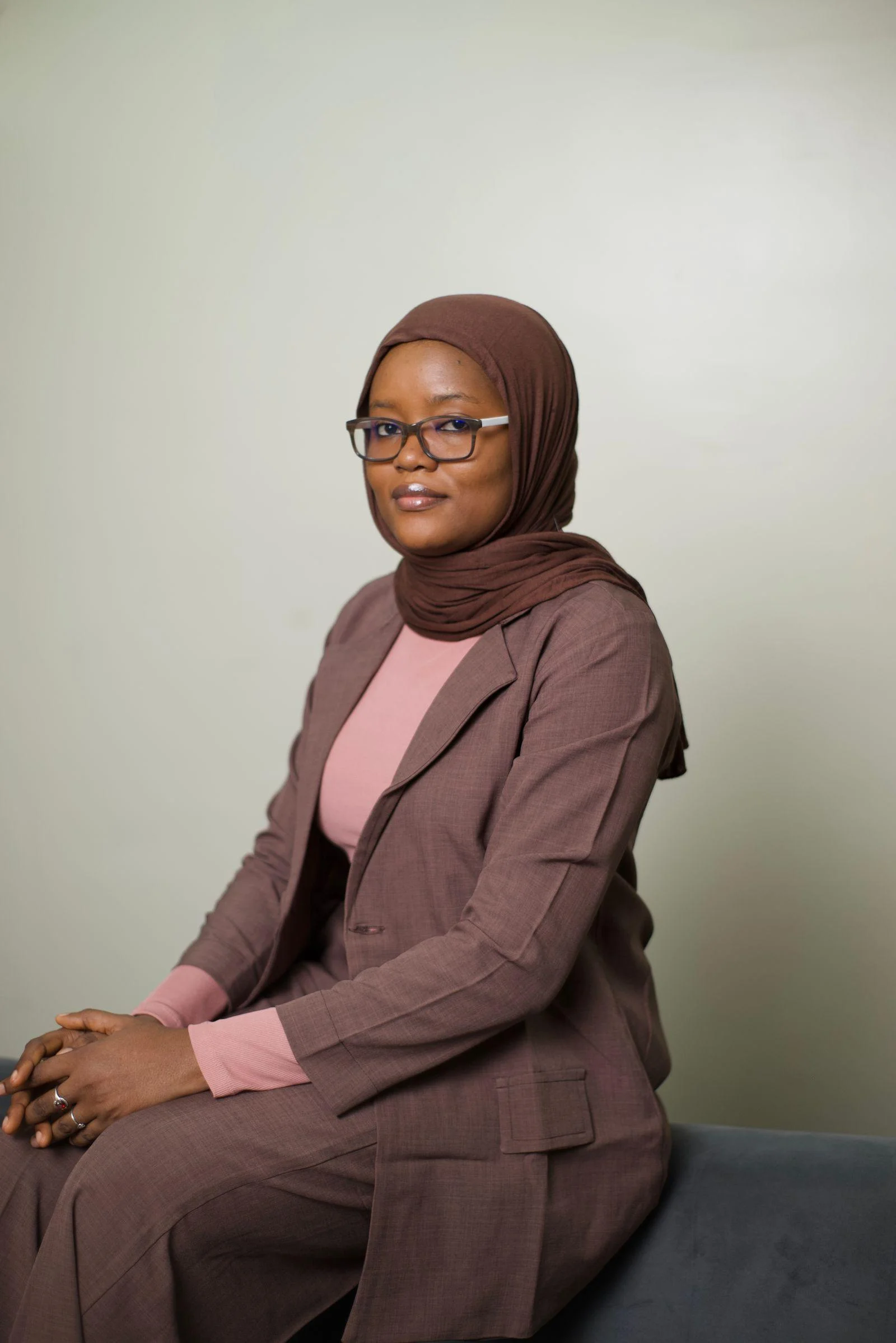 A woman wearing glasses and a brown headscarf sits for a portrait in Abuja